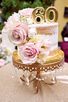 a white and gold cake with pink flowers on the top is sitting on a table