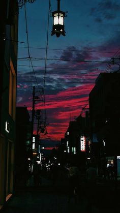 the sky is red and purple as people walk down the street at night in an urban setting