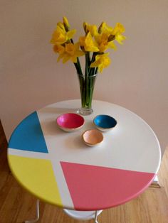 a vase with yellow flowers sitting on top of a table next to two colorful bowls