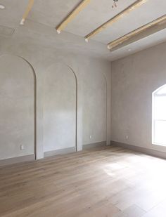 an empty room with white walls and wood flooring is pictured in this image, there are three arched windows on the far wall