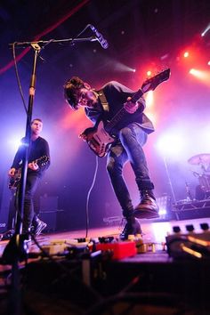 two men on stage playing guitars and singing into microphones while another man stands behind them