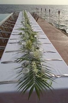 a long table is set up with silverware and flowers on it, overlooking the ocean