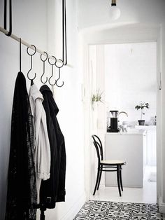 a black and white photo of a hallway with clothes hanging on the wall, chairs in the background