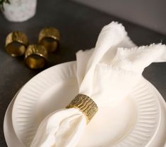 the napkin is on top of the white plate with gold napkin rings next to it