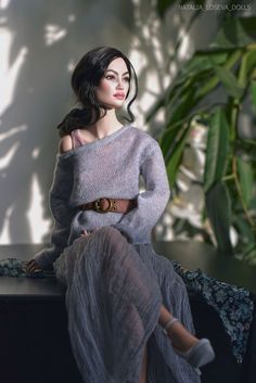 a woman sitting on top of a table wearing a gray sweater and grey skirt with her legs crossed