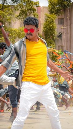 a man in yellow shirt and white pants with red sunglasses on his face standing next to other people