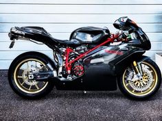 a black and red motorcycle parked in front of a garage door with yellow rims