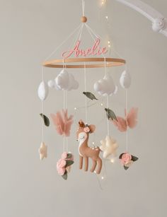 a baby mobile with pink and white decorations hanging from it's sides, including a deer