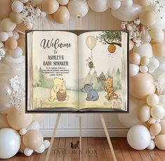 an open book with winnie the pooh on it and balloons around it in front of a backdrop