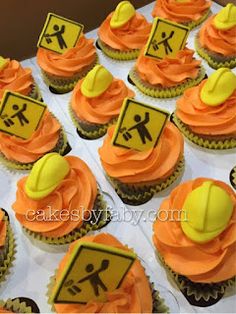 cupcakes with orange frosting and yellow construction hats on top are arranged in rows