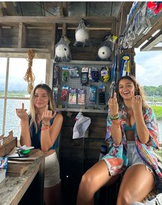 two women sitting at a table in front of a window and making the peace sign