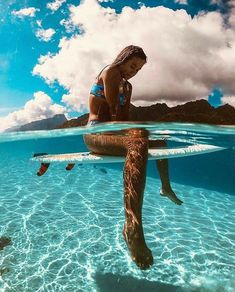 a woman is sitting on a surfboard in the water while another person swims behind her