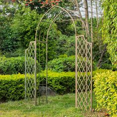 an iron garden arbor in the middle of a grassy area with bushes and shrubs behind it