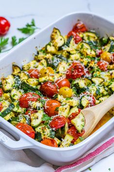 a casserole dish with tomatoes, zucchini and spinach