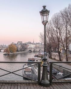 a lamp post sitting on the side of a bridge next to a river with boats in it