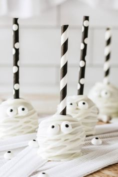 three halloween cake pops decorated with white frosting and black striped straws, one has eyes on it