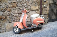 an orange scooter parked next to a stone wall