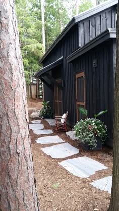 a small black cabin in the woods with steps leading up to it's door