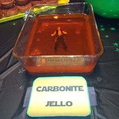 a plastic container filled with jello sitting on top of a table next to cupcakes