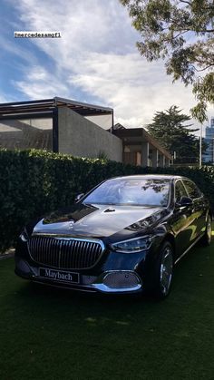 a black car parked in the grass next to some bushes and trees on a sunny day