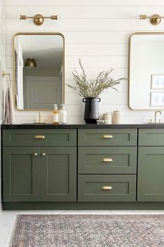 a bathroom with green cabinets and two mirrors on the wall, one has a plant in it