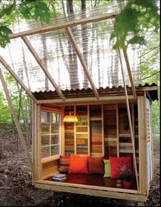 a small wooden house in the woods with lots of pillows on it's bed