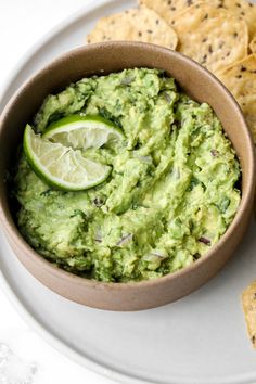 a bowl filled with guacamole next to tortilla chips on a plate