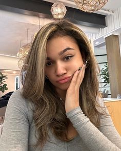 a woman sitting at a table with her hand on her face and looking into the camera