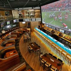 a sports bar with many tables and chairs in front of a big screen tv that is on the wall