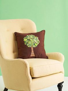 a chair with a pillow on it in front of a green wall and a tree