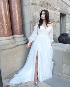 a woman in a white dress leaning against a wall