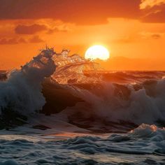 the sun is setting over an ocean with waves crashing in front of it and some clouds