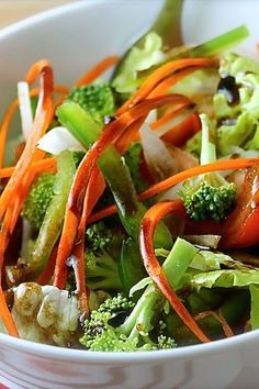 a salad with carrots, broccoli and onions in a white bowl on a table