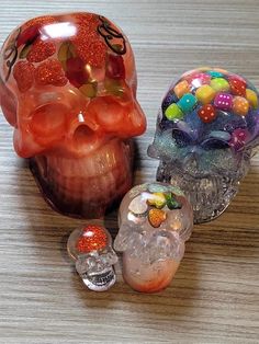 three different colored glass skulls sitting on top of a wooden table next to each other