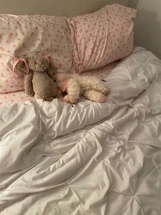 two stuffed animals laying on top of a bed with white sheets and pillows in front of them