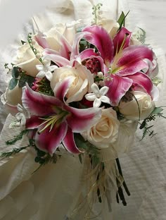 a bridal bouquet with white roses and pink lilies on a bed in the sunlight