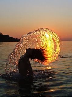 a woman is in the water with her hair blowing back and holding onto an object