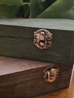 two wooden boxes sitting next to each other on top of a wood table with plants in the background