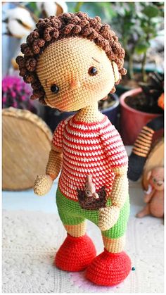 a crocheted doll is standing on the floor in front of potted plants