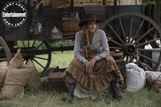 a woman sitting on the ground in front of an old fashioned wagon and other items