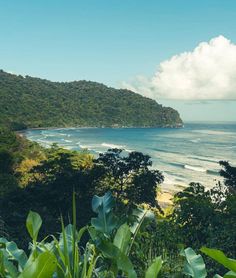 the ocean is surrounded by lush green trees and hills, with clouds in the sky