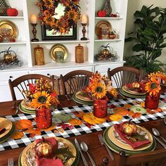 a dining room table set for thanksgiving with sunflowers and pumpkins in vases