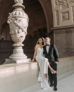 a bride and groom posing for a photo in front of a large white urn