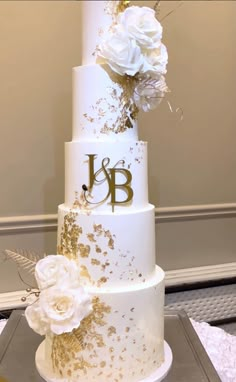 a three tiered white and gold wedding cake with flowers on top is decorated with monograms