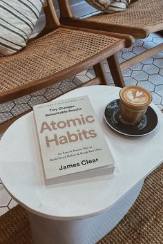 a cup of coffee sitting on top of a table next to a book and chair