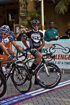 two bicyclists riding on the same bike in front of a group of people