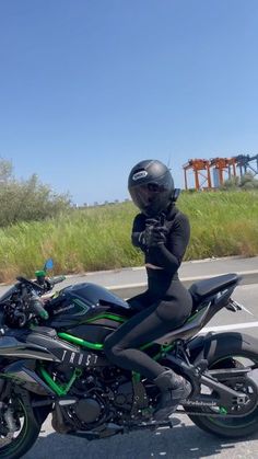 a person in black is sitting on a green and black motorcycle while wearing a helmet