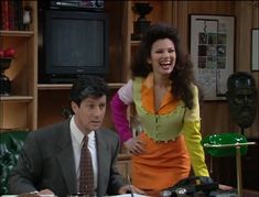 a man and woman sitting at a table in front of a television set with the tv on