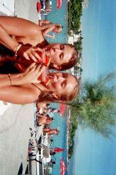 two young women standing next to each other on the beach looking at their cell phones