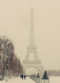 the eiffel tower is covered in snow as people walk on a sidewalk near it